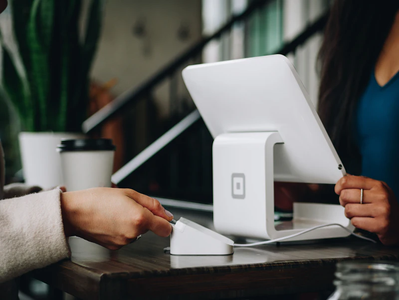 A customer taps a card on a counter payment reader while a shop employee holds the tablet register.